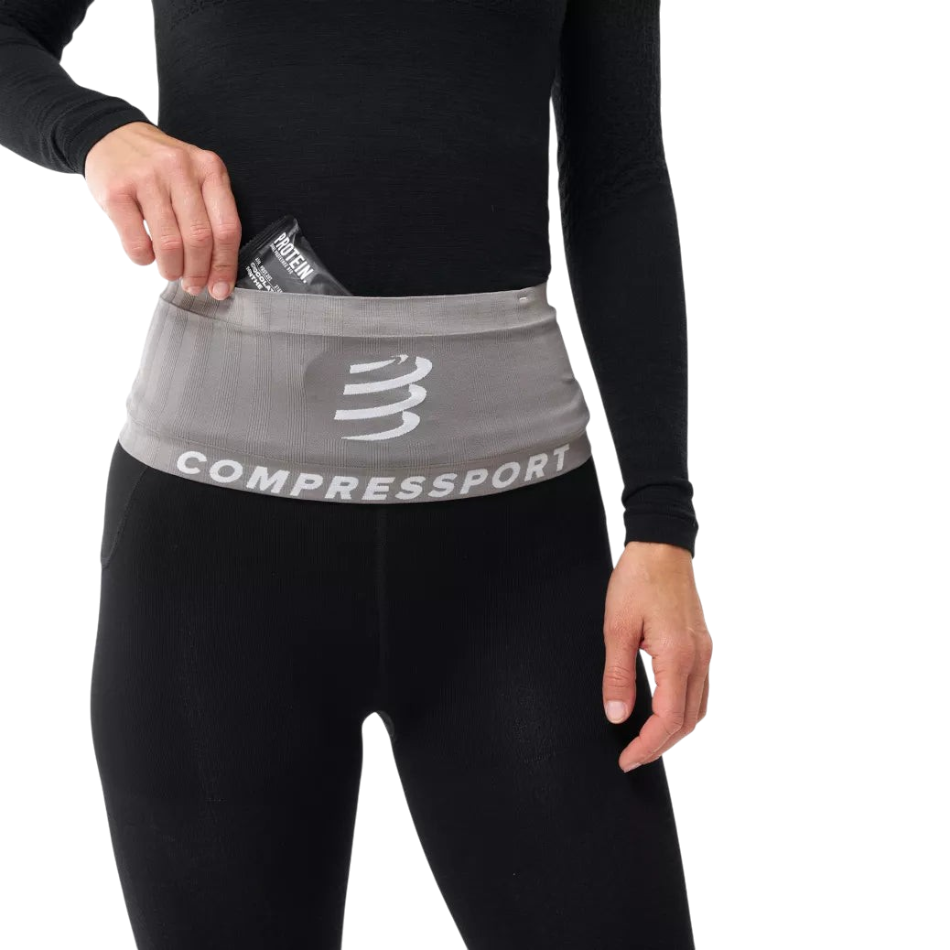 Up & Running Compressport Free Belt 2.0 in grey worn around the waist with a runner accessing a nutrition gel pocket.