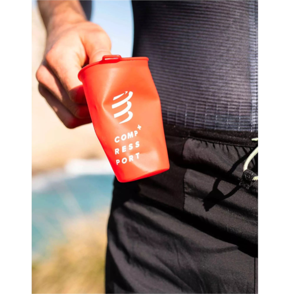 Up & Running Compressport red collapsible trail running cup held by a runner in a vest