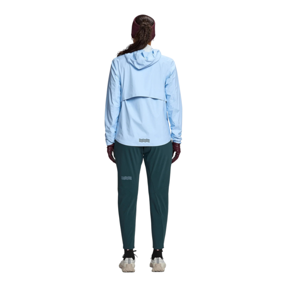 Back view of a runner wearing a light blue Janji Rainrunner Pack Jacket from Up & Running with dark green leggings.