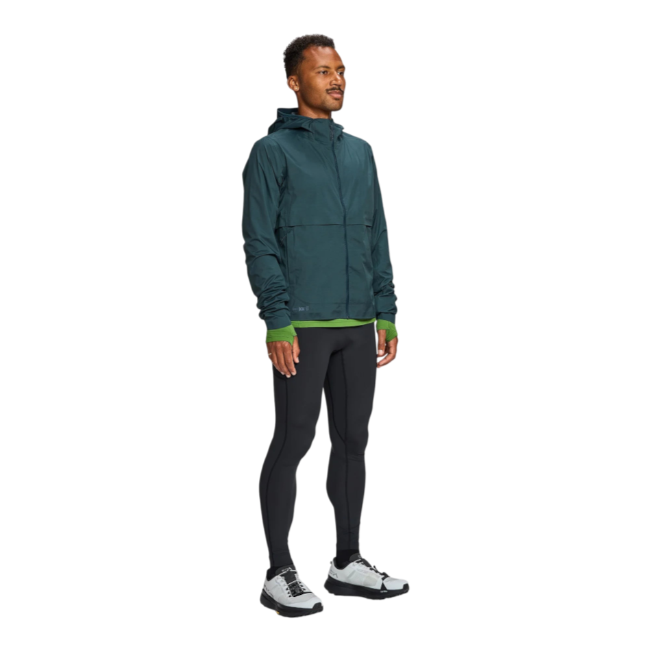 Up & Running model wearing a dark teal Janji Rainrunner waterproof running jacket with hood and black leggings.
